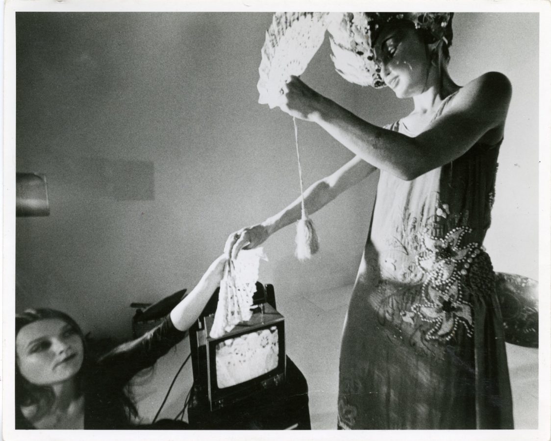 Jonas wearing a mask and feather headdress while holding a fan and giving a handkerchief to another performer