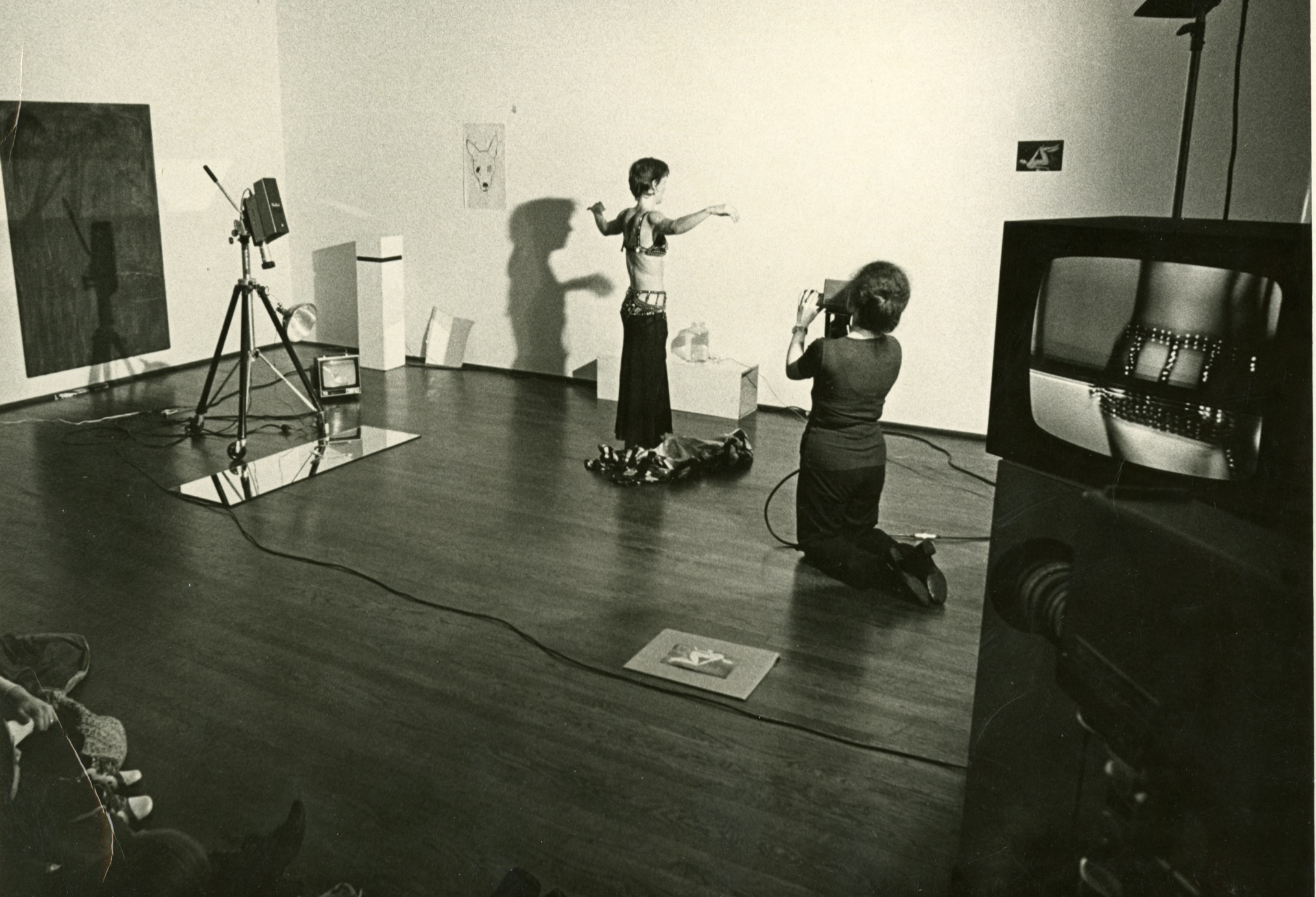 Jonas stands with her arms extended in front of a camerawoman while the audience watches from the floor.