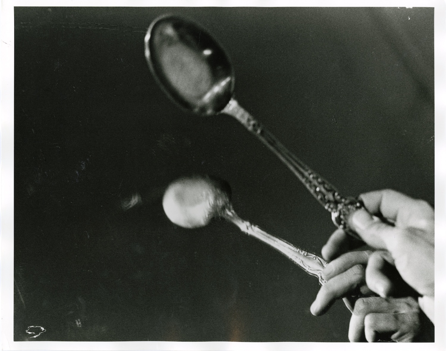 Photograph of a performer’s hand tapping a spoon against a mirror