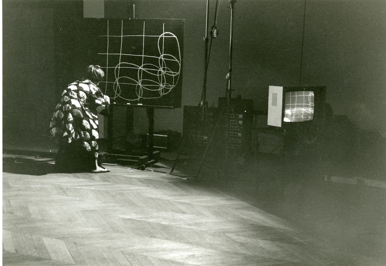 Jonas drawing on a chalkboard with a video monitor to her right