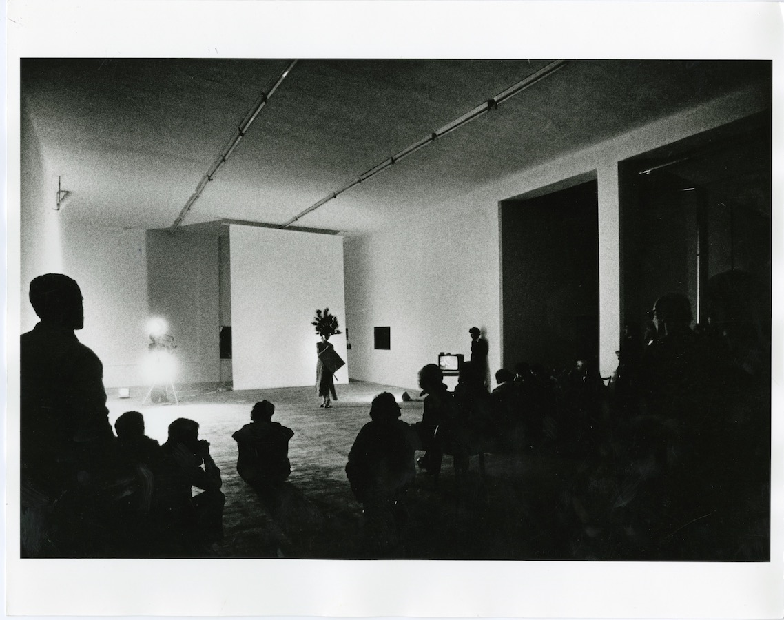 Audience watching Jonas wearing a peacock-feathered headpiece and dress while holding a mirror