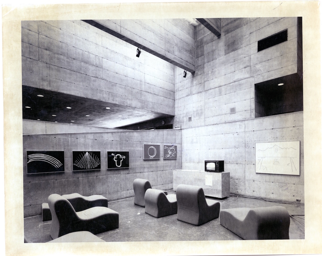 Various lounge chairs are placed in front of a TV monitor, on the walls are various drawings.