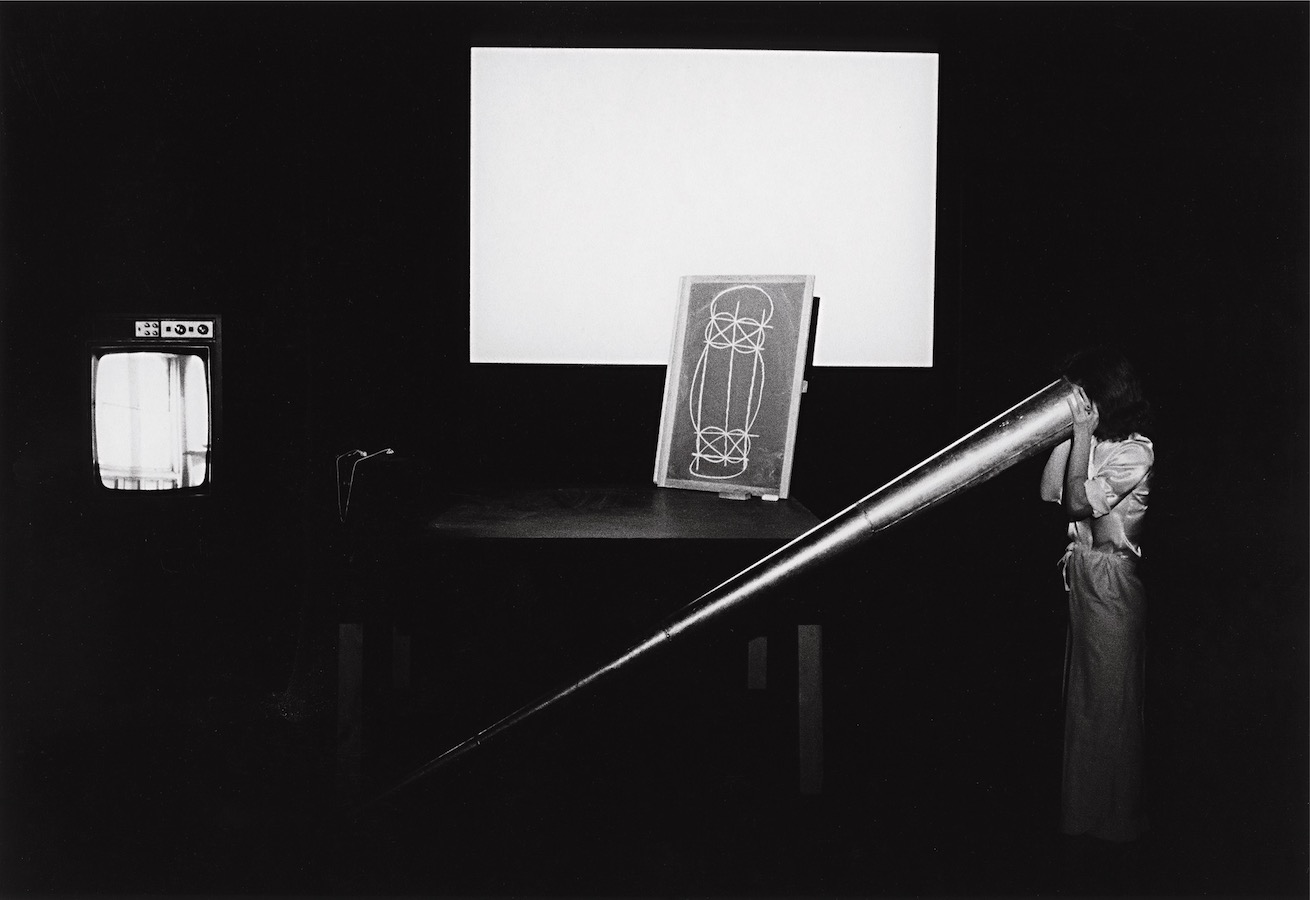 Jonas looking into a giant cone. A drawing is placed on a table with a projection behind it; to the left is a TV monitor.