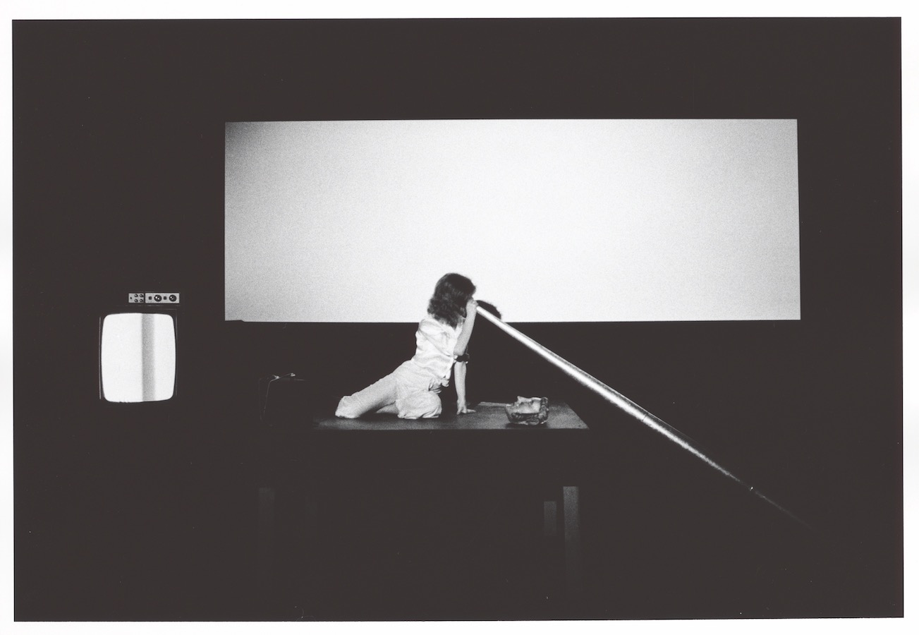 Jonas on top of a stage looking into a large cone; to the left is a TV monitor.