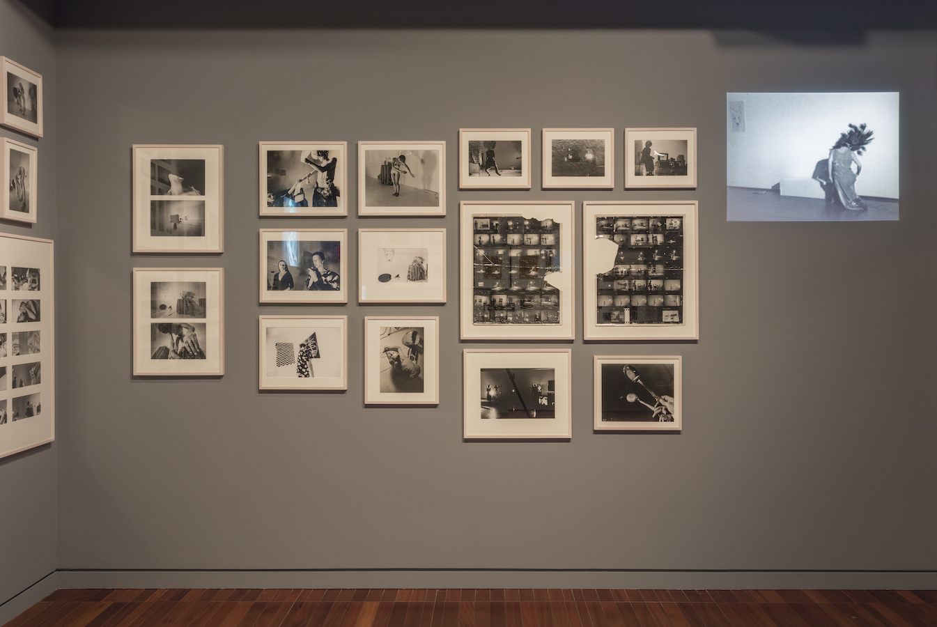 Various framed photographs and photographic contact sheets and a projection from Jonas’s performances are displayed on a wall. There is a bench in the middle of the room.