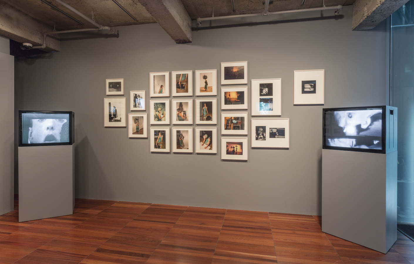 Framed photographs from Jonas’s performances are displayed on a wall; there are also two TV monitors on stands.