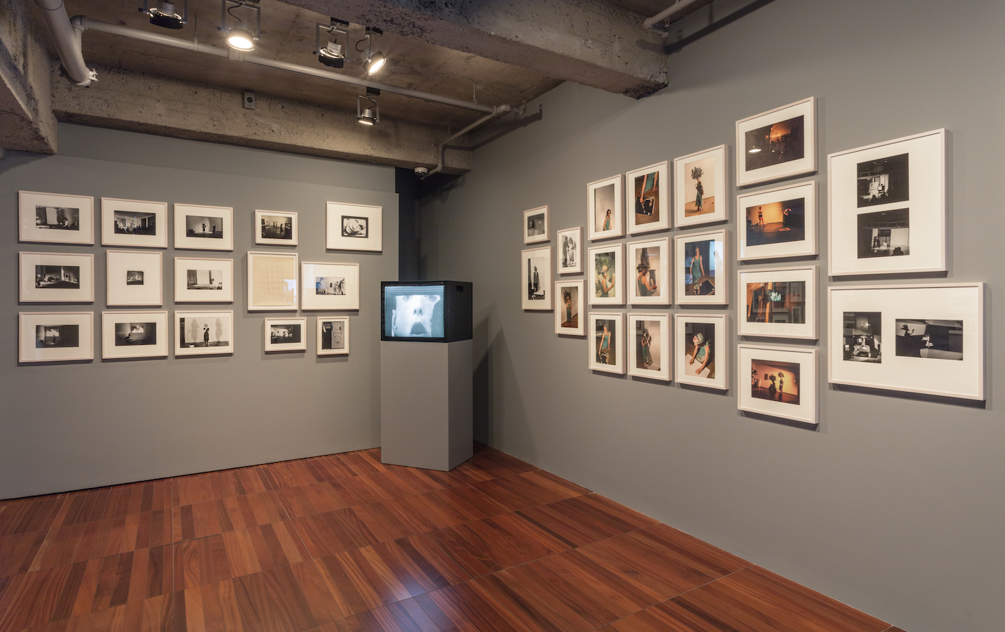 A TV monitor on a stand is placed in the corner of the room; on the surrounding walls are framed photographs from Jonas’s performances.