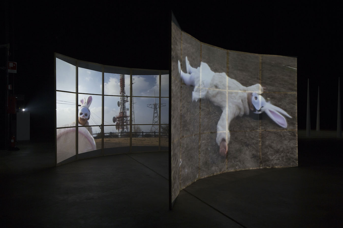 Two video projections of a figure in a rabbit suit on curved screens