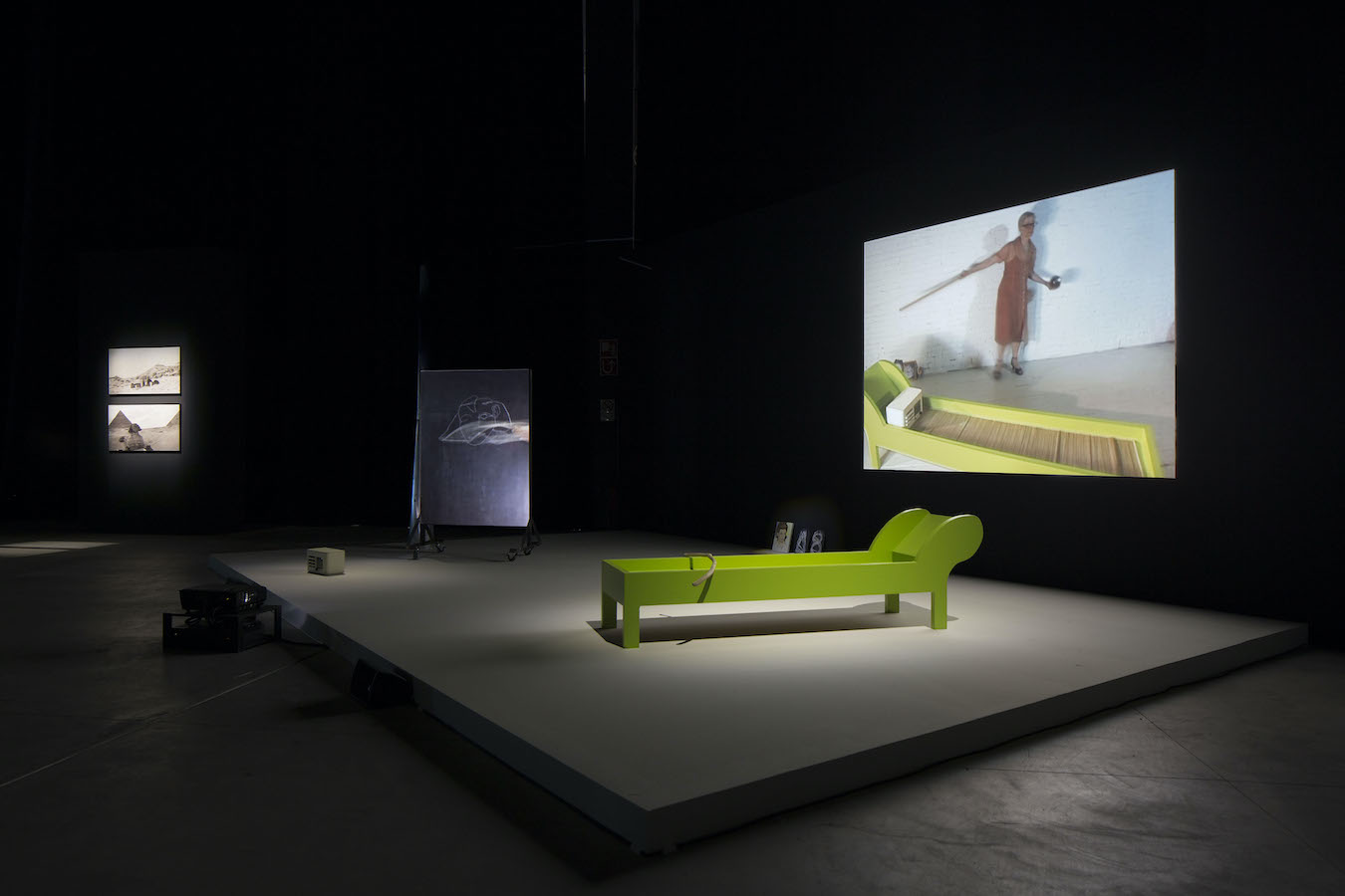 A lounge chair and a chalkboard are placed on a stage in front of a video projection.