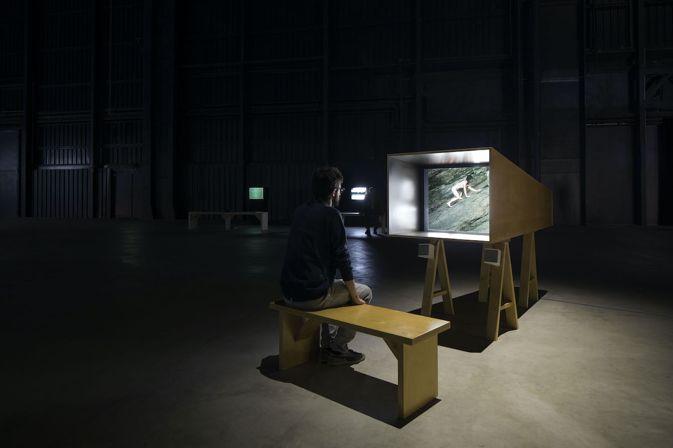 A figure sitting on a bench in front of a TV monitor