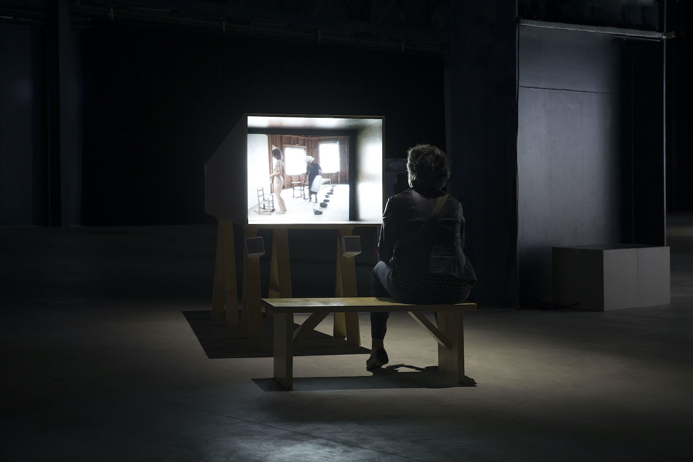 A figure sitting on a bench in front of a TV monitor