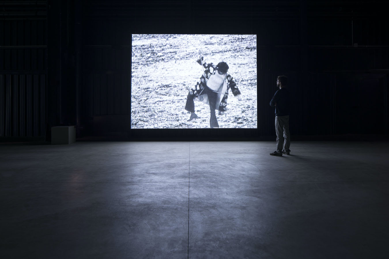 A figure stands in front of a video projection