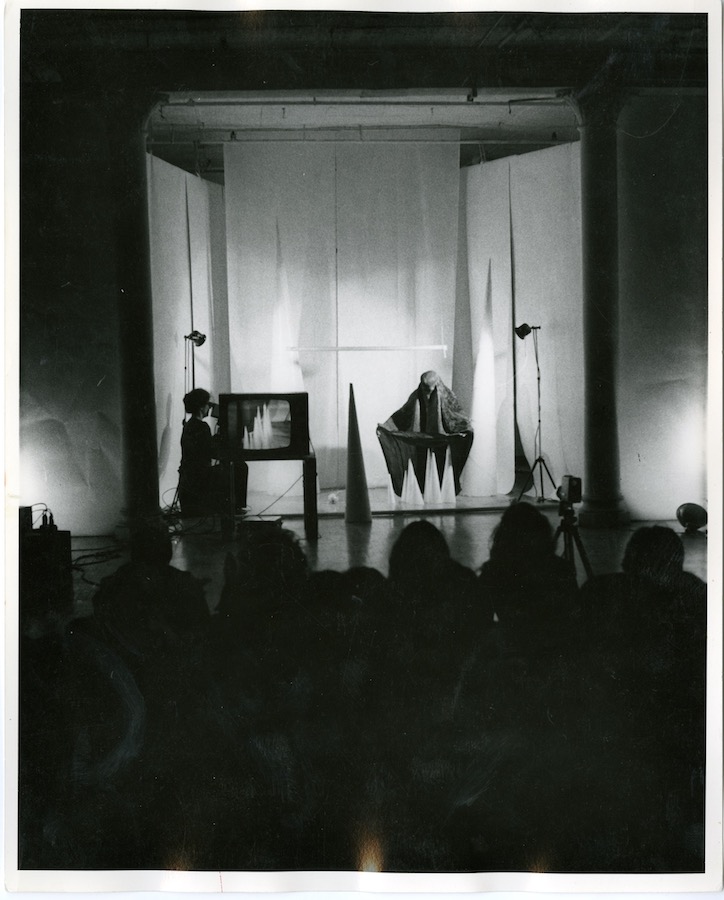 Jonas performs in front of a crowd; there are various sized cones, a camerawoman filming Jonas, and a TV monitor on a table displaying the video to the audience.