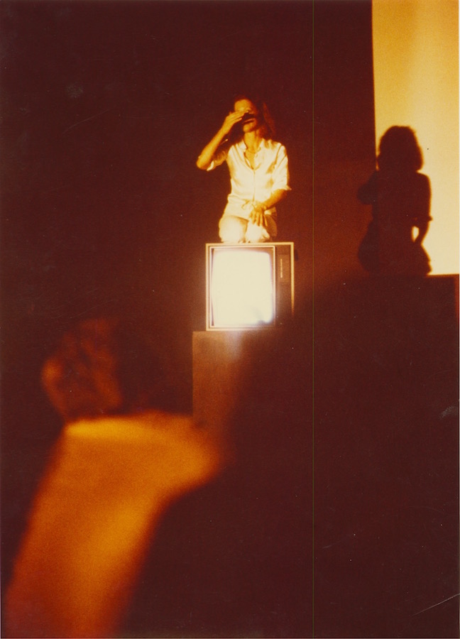 View from the audience of Jonas sitting on top of a TV monitor with her hand covering her eyes