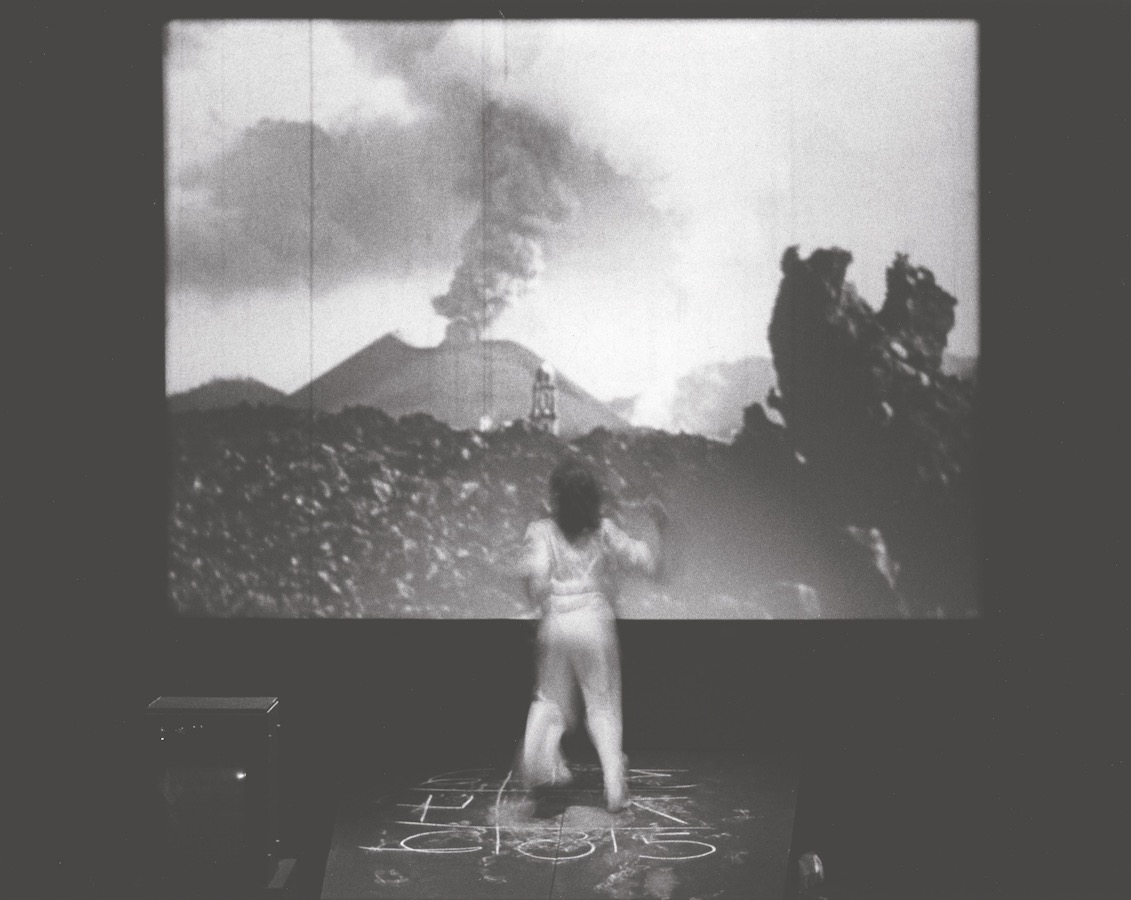 Jonas standing on top of a chalk drawing facing a projection of an erupting volcano