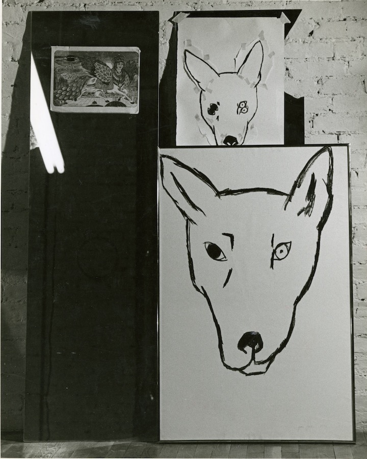 Two drawings of a dog’s head, one with two eyes and another with four eyes, hang next to a mirror.