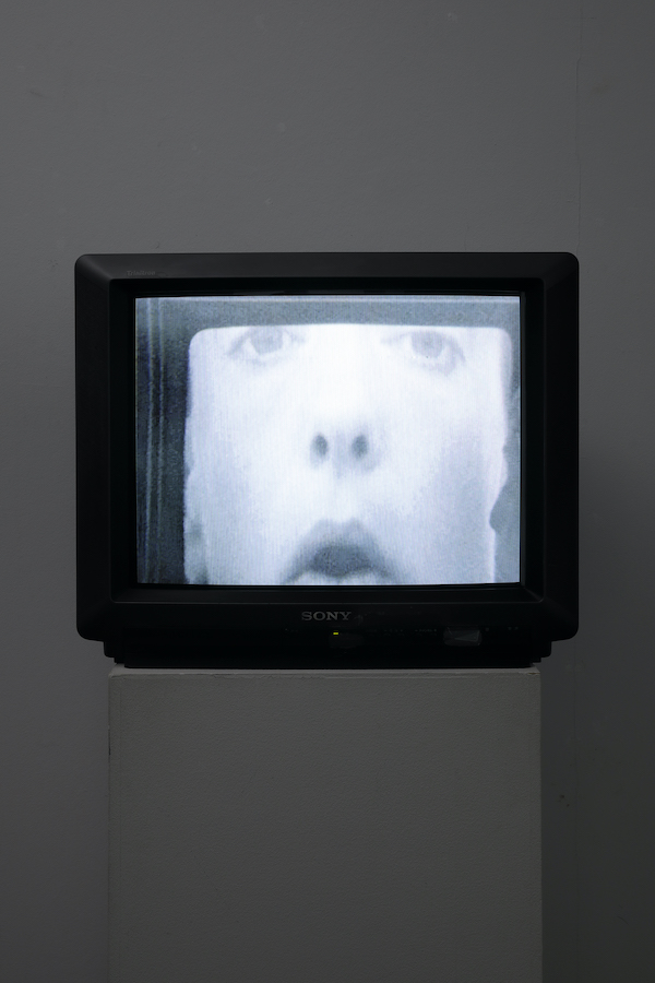 A TV monitor on a stand displaying a closeup of a woman’s face.