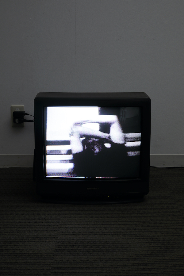 A TV monitor on the floor displaying a performer holding their arms.