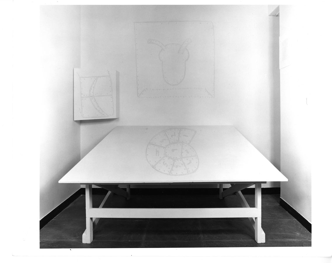 A table with a lightly drawn 1 - 9 number wheel on top, behind the table are two drawings.