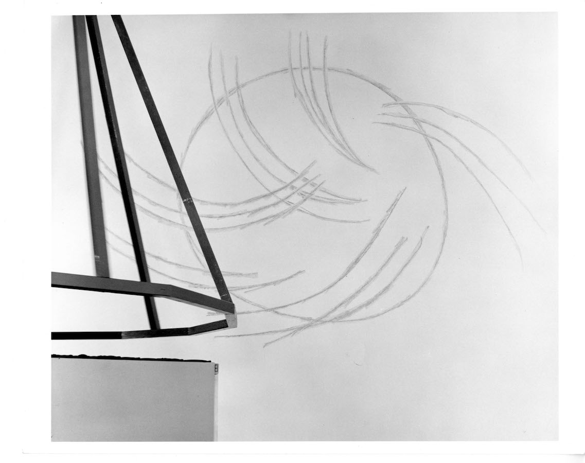 In the foreground is a metal frame in the shape of a cone, in the background is a drawing of a circle with various lines coming out.