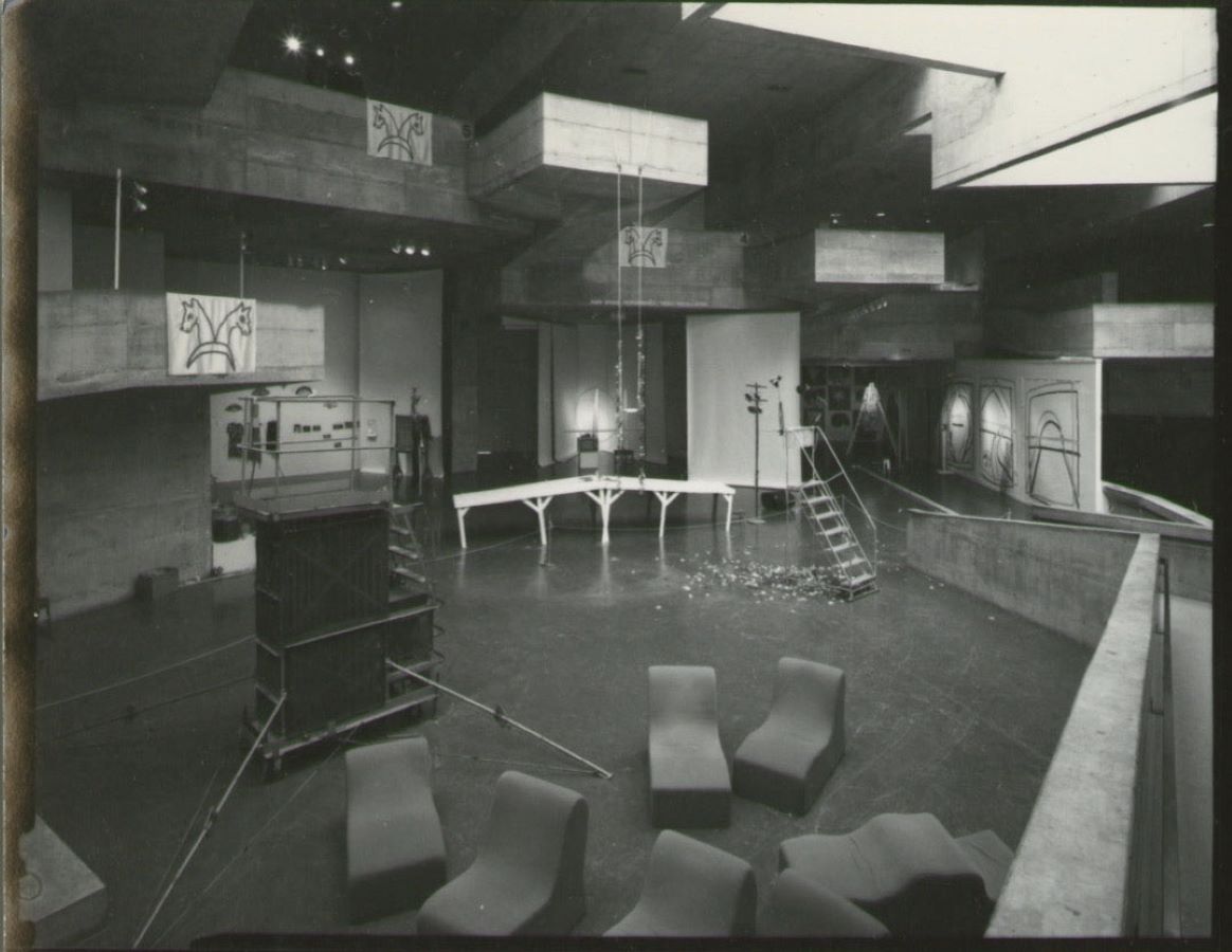 A room filled with various props, drawings, a swing hanging from the ceiling, a bridge, a ladder, and lounge chairs.