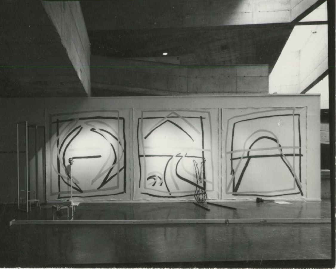 A wall with three drawings, to the left is a pole with a mask on it.