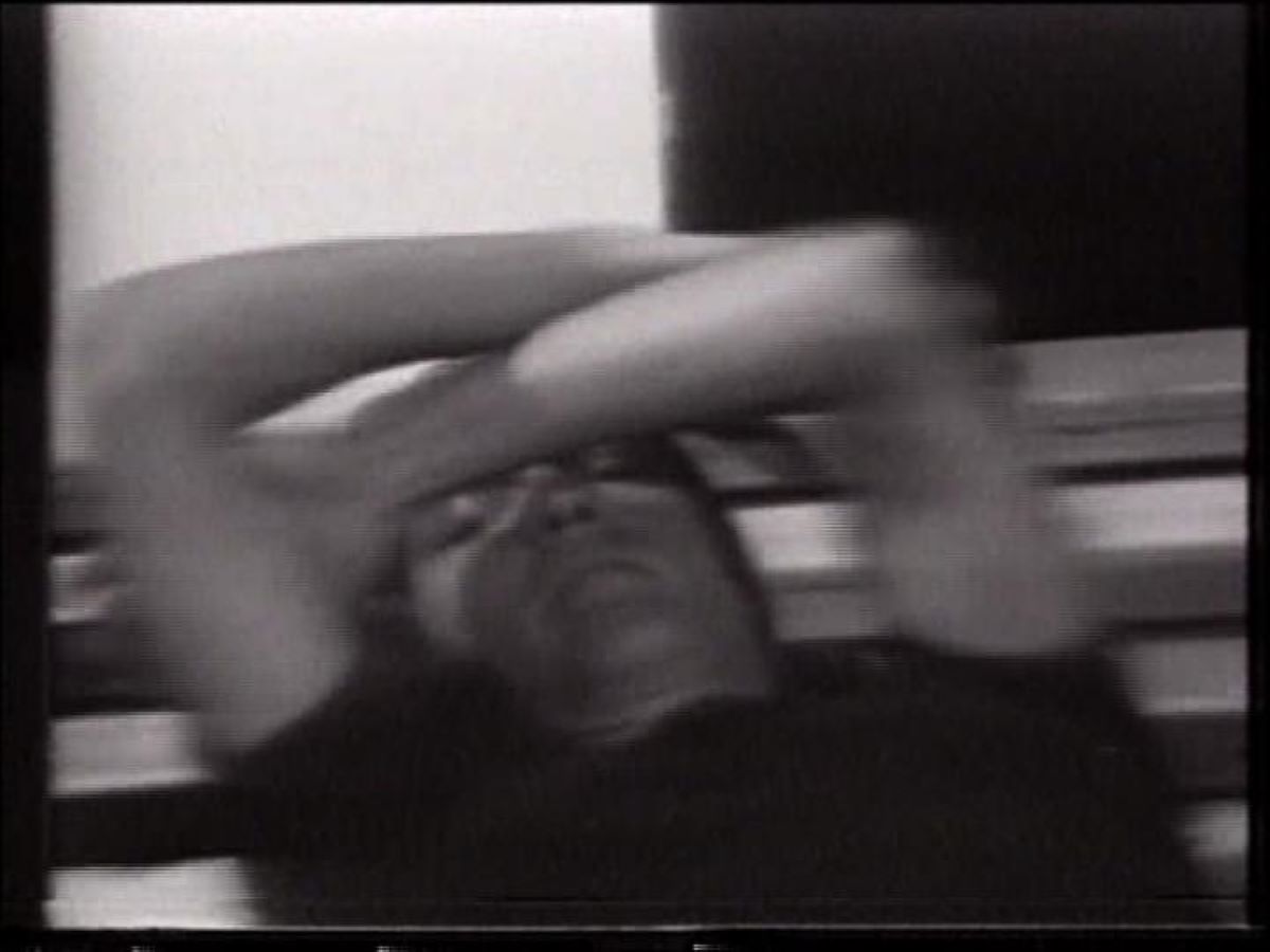 Video still of a figure laying down with their arms crossed over their head.