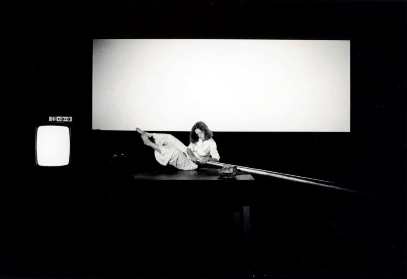 Jonas on top of a table holding a large metal cone; in the background is a blank screen and a TV monitor.