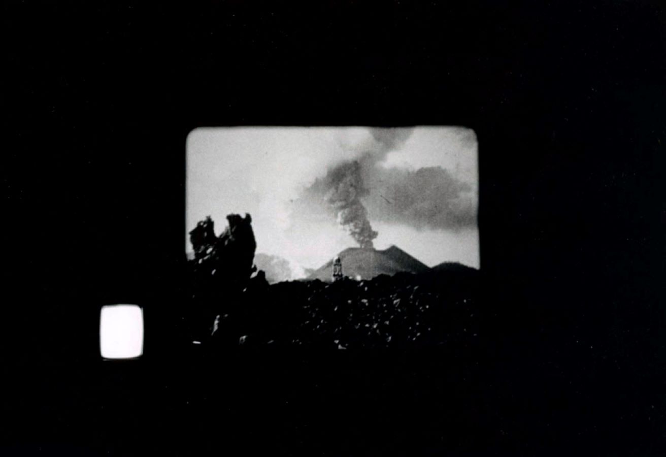 Projection of a volcano erupting, to the left is a TV monitor