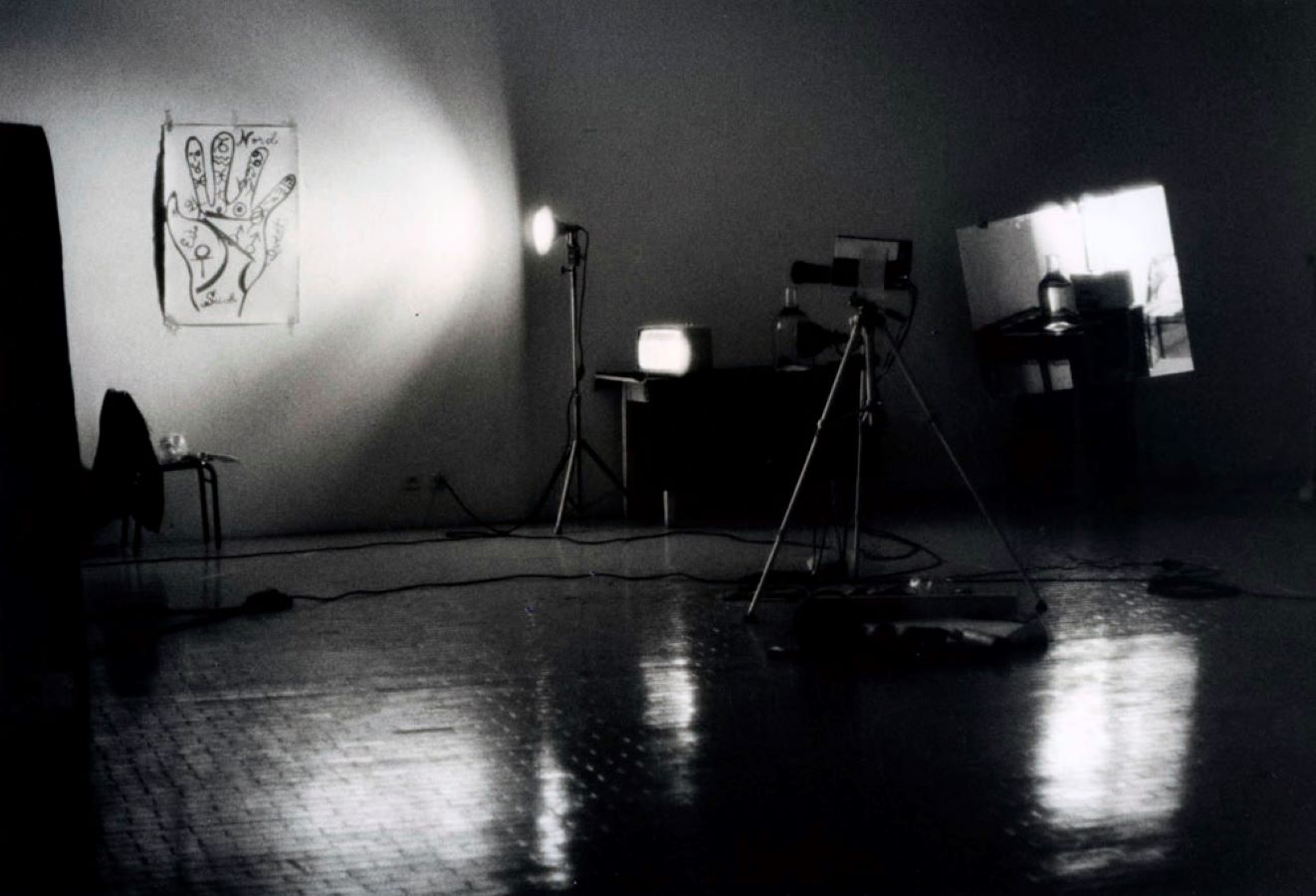 A drawing of a hand is taped to the back wall and is illuminated by a light. There is a camera on a tripod pointing at the drawing.