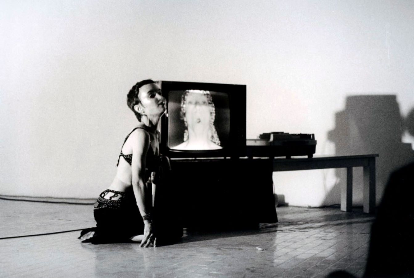 Jonas, wearing a mask, kneels next to a TV monitor on a table