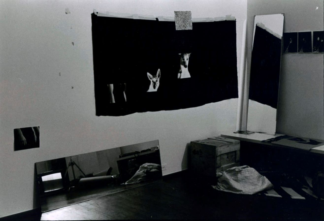 A corner of a room with two full-length mirror, a wooden box, various images, and a black sheet hanging on the wall