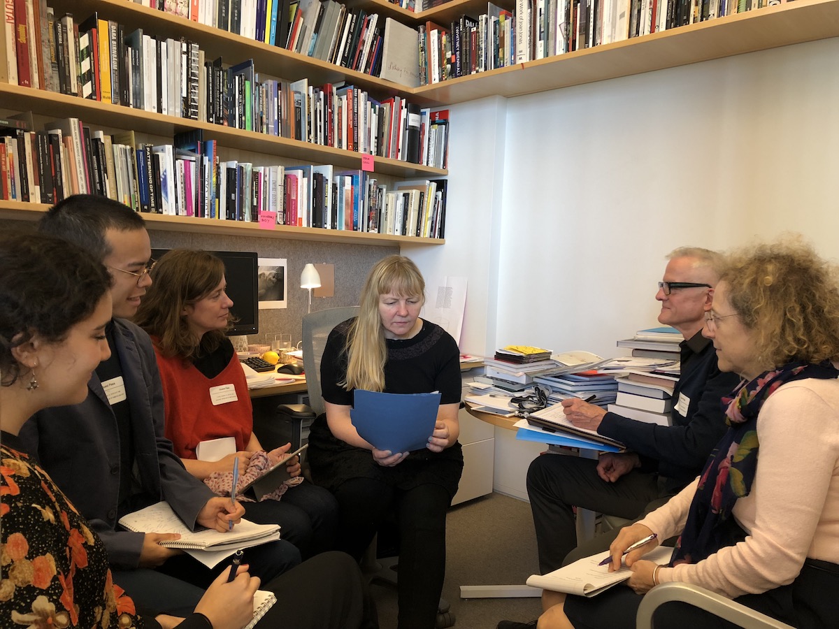 Six people sitting in an office with various books on wall shelves.