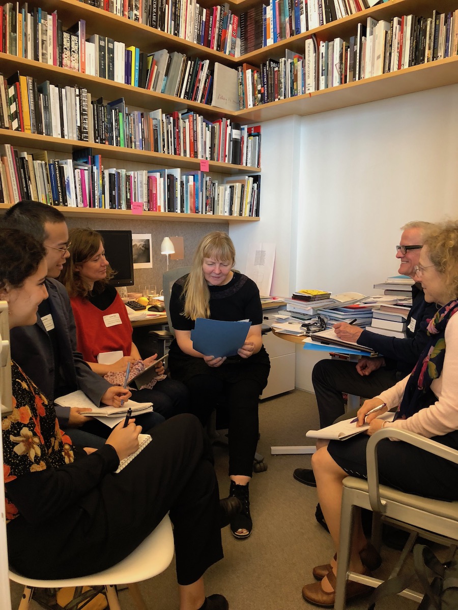 Six people sitting in an office with various books on wall shelves.