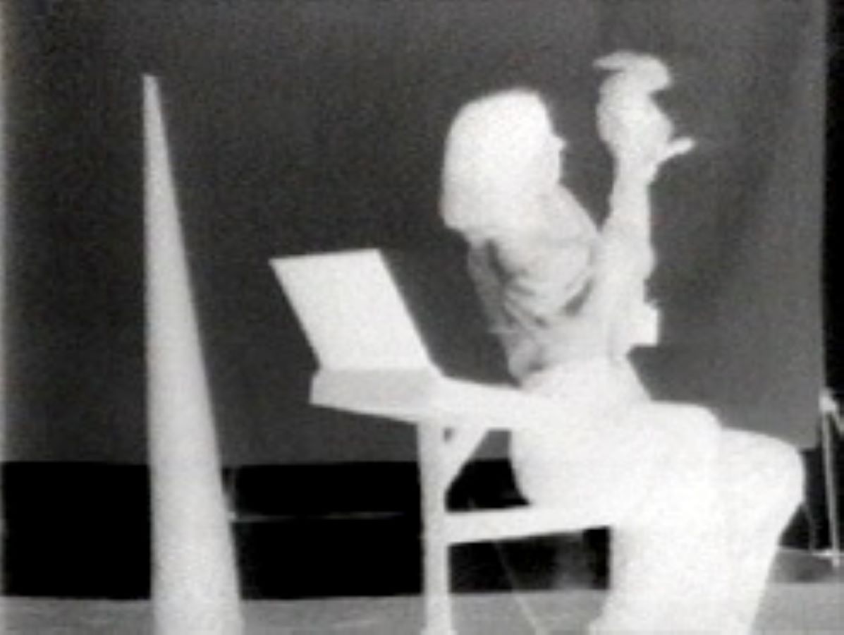 Video still with negative image of Jonas sitting next to an open box and holding a rabbit, to the left is a large cone.