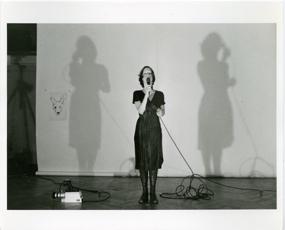 Jonas standing in front of a white backdrop with a drawing of a dog’s head while holding a microphone up to her mouth